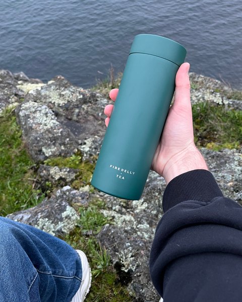 A green Firebelly travel mug held up by the water