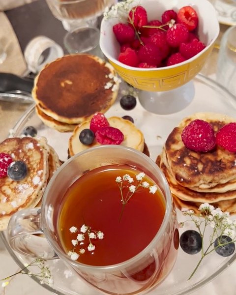 A cup of tea on a table of pancakes and berries