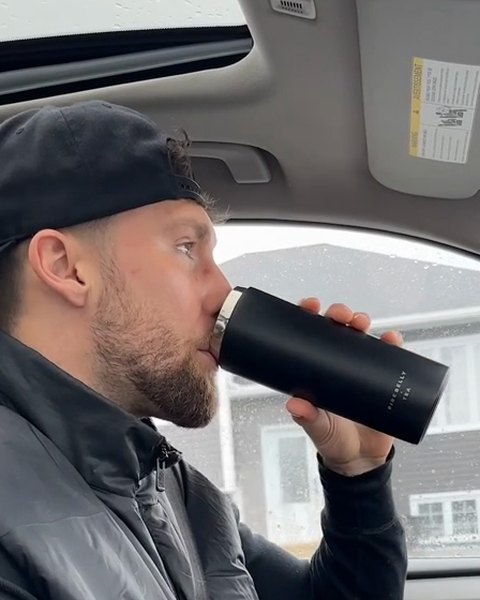 A man drinking from a black travel mug in his car